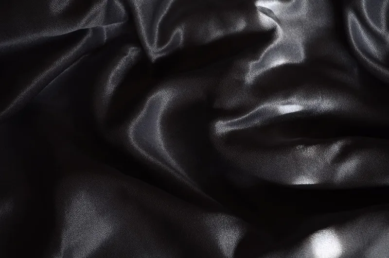 Deep charcoal satin fabric in soft folds, shot as an abstract still life