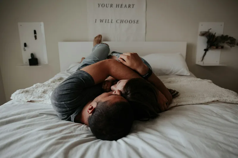 A couple cuddling together in bed in soft morning light, talking closely in a relaxed, trusting moment