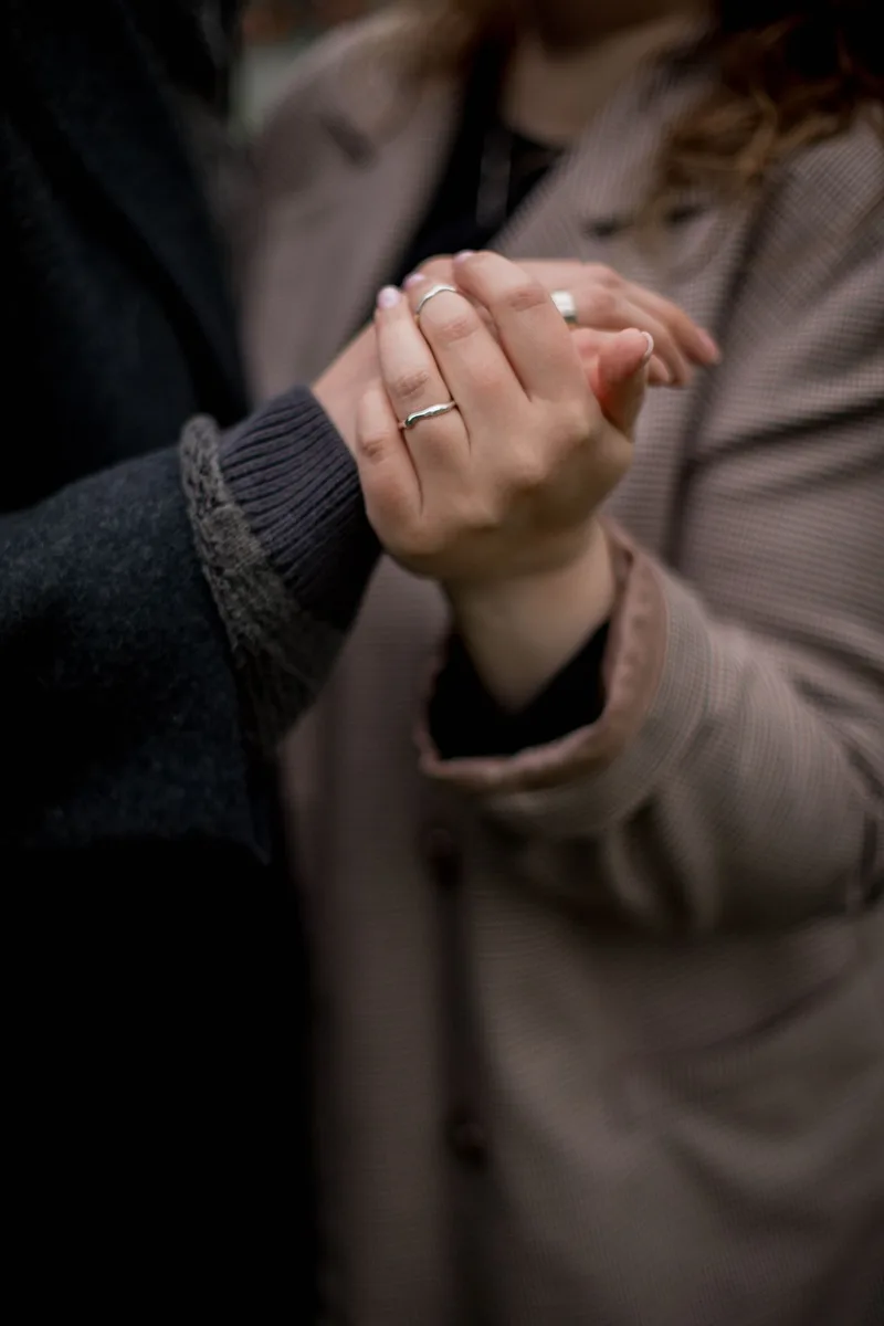 A close-up of a couple's intertwined hands with wedding rings, resting together in soft light, a modest non-explicit image of two people holding hands