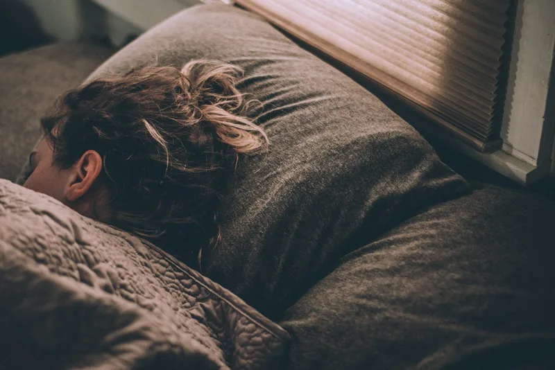 A person sleeping peacefully in bed under blankets, illustrating the sleep benefits of orgasm