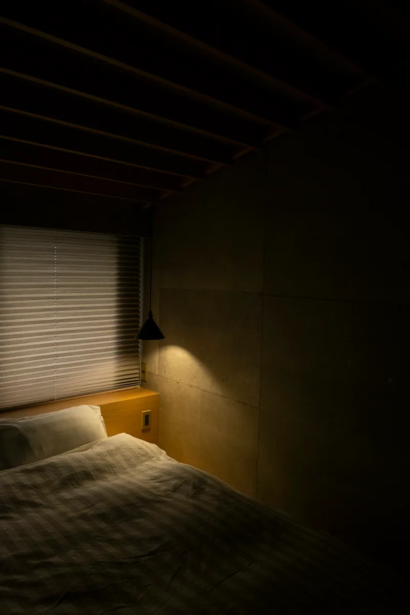 White bed linen beside window blinds in soft daylight, a calm and private bedroom scene